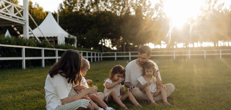 Family sitting on grass enjoying leisure time outdoors, with sun setting in the background.