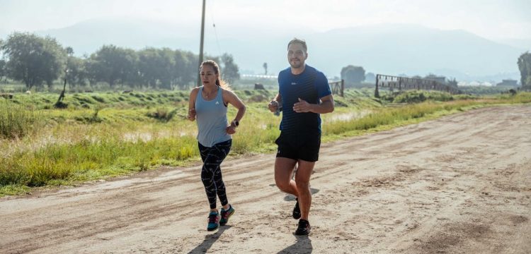Active couple jogging on a dirt road in a scenic rural area under the bright sun.