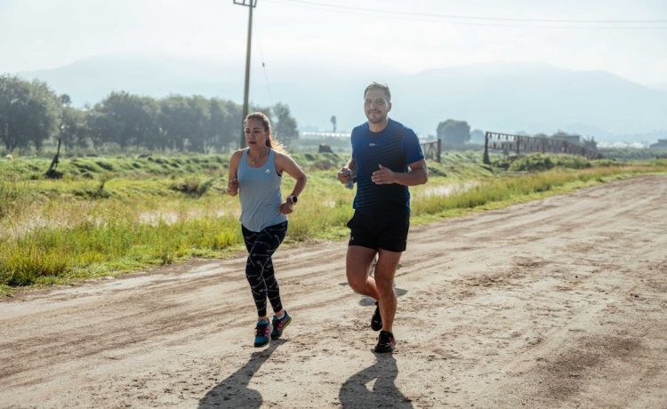 Active couple jogging on a dirt road in a scenic rural area under the bright sun.